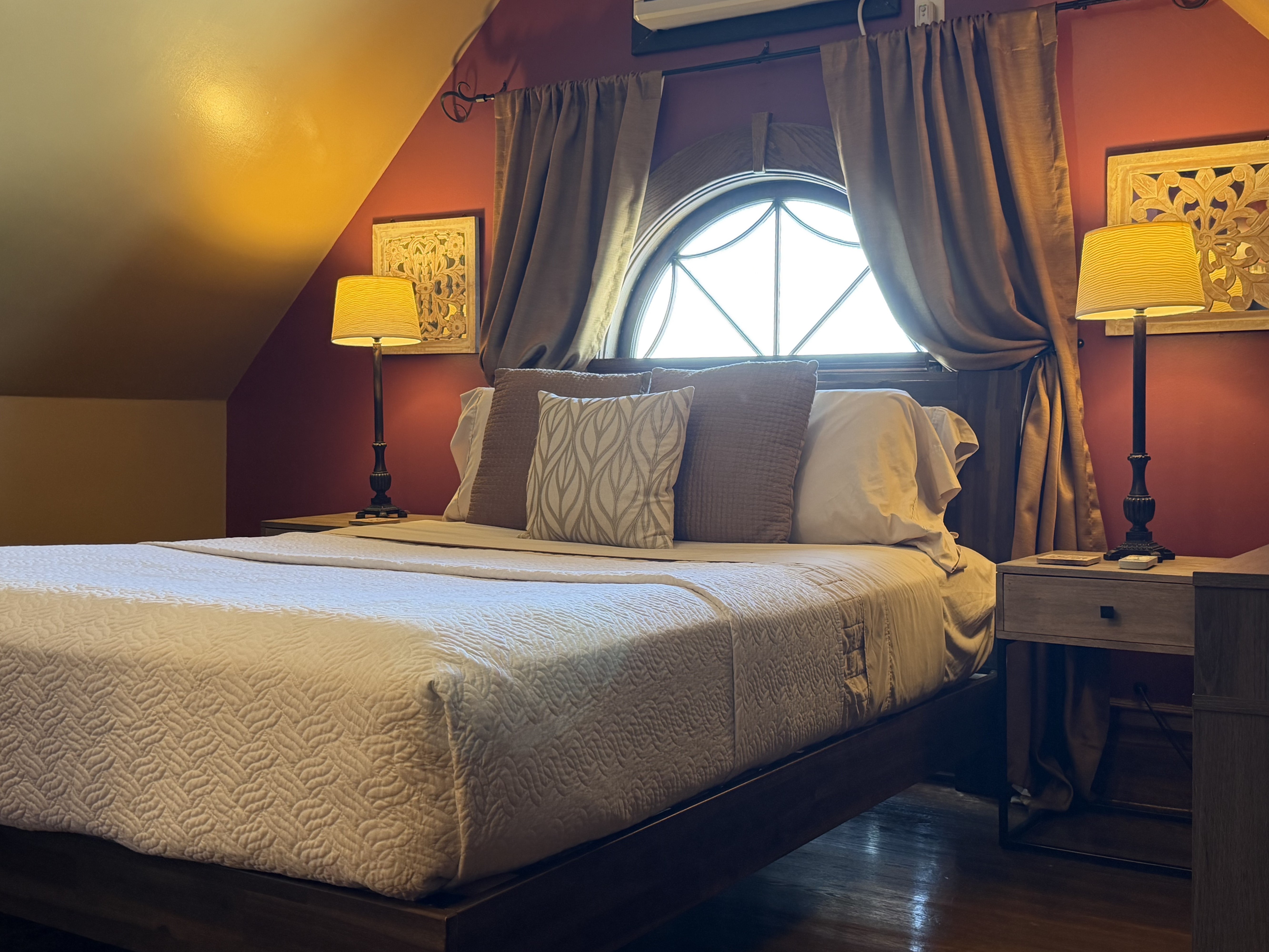 Room with a queen size bed, angled ceilings with a unique picture window.