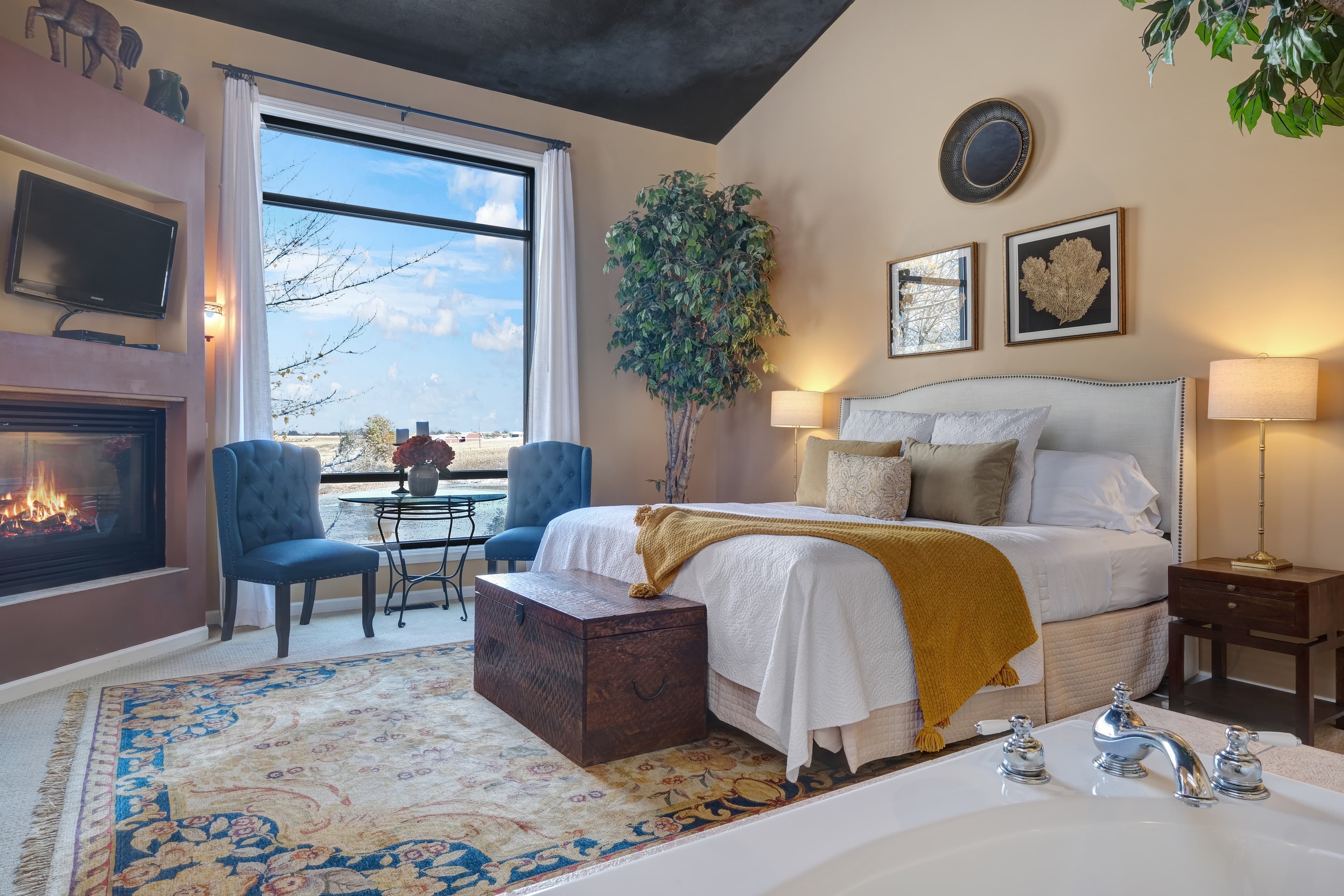 Suite with a king size bed, seating area by the fireplace with a large window over looking the pond.