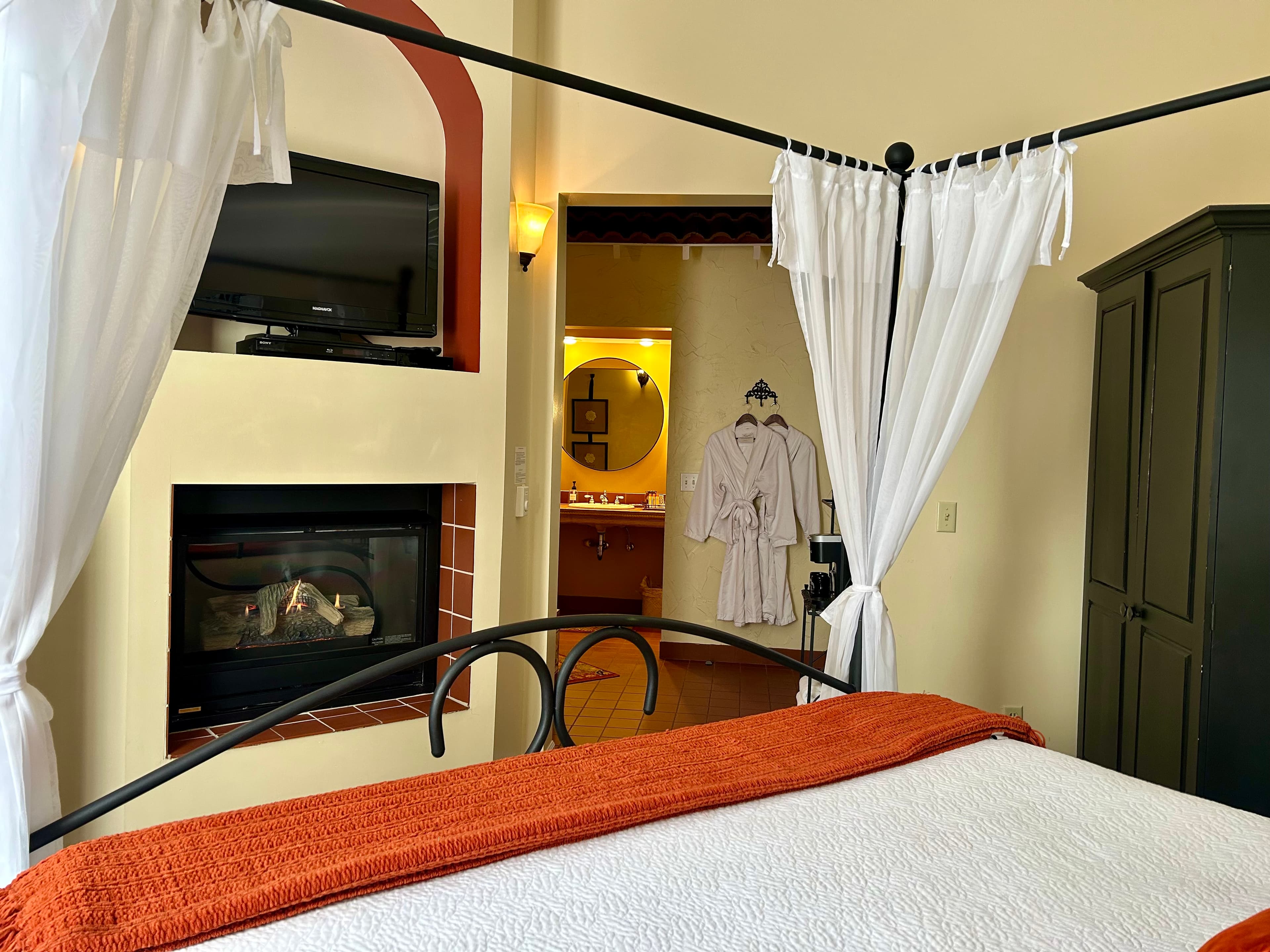 Suite with a king canopy bed with a seating area, fireplace and TV