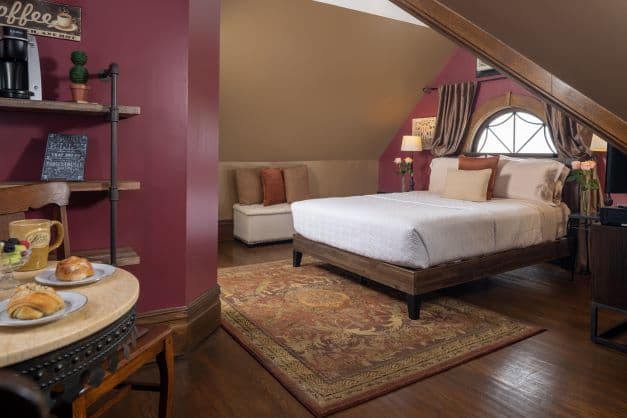 Room with a queen size bed, angled ceilings with a unique picture window.