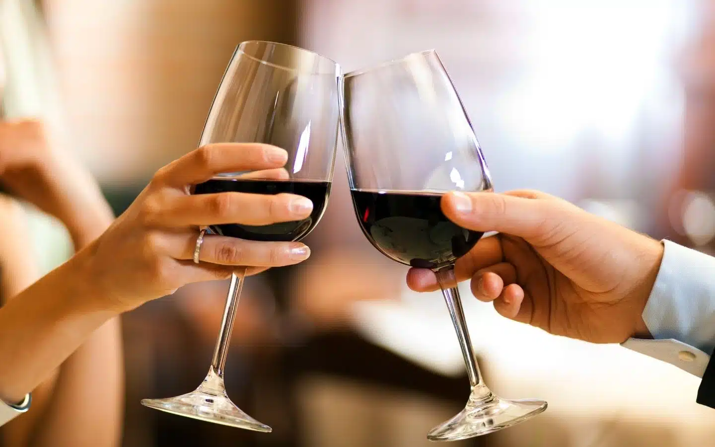 Two hands clink wine glasses filled with red wine.