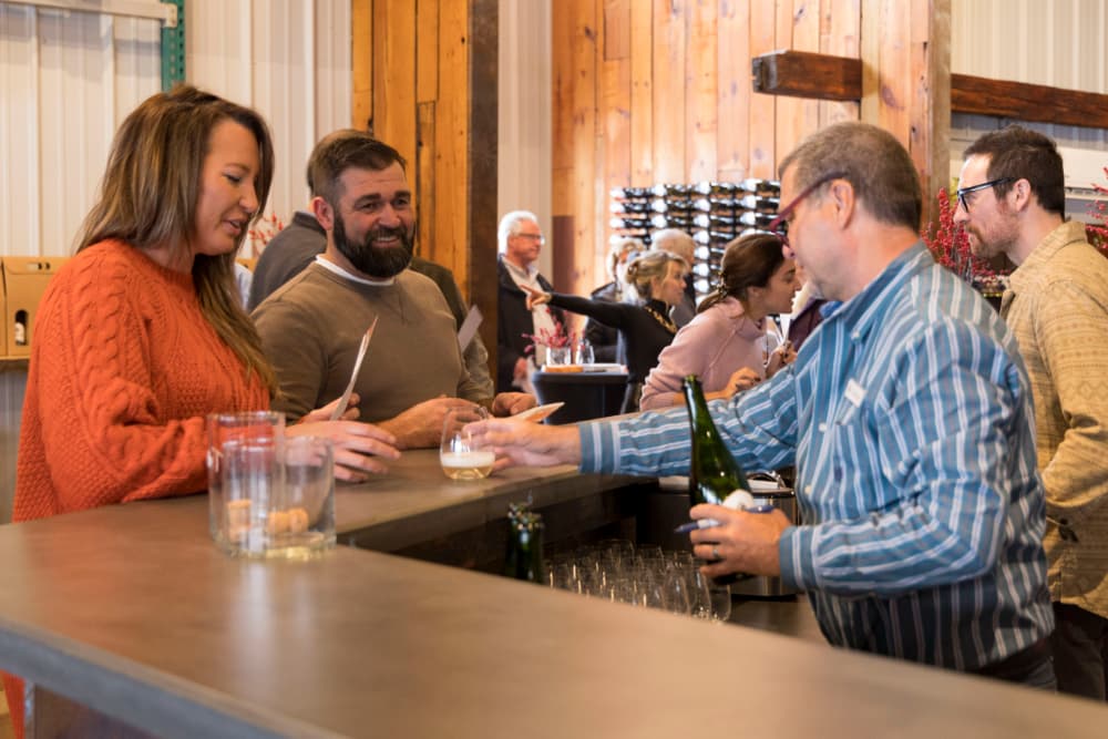 A lively bar scene featuring people engaging with bartenders and enjoying drinks in a rustic setting.
