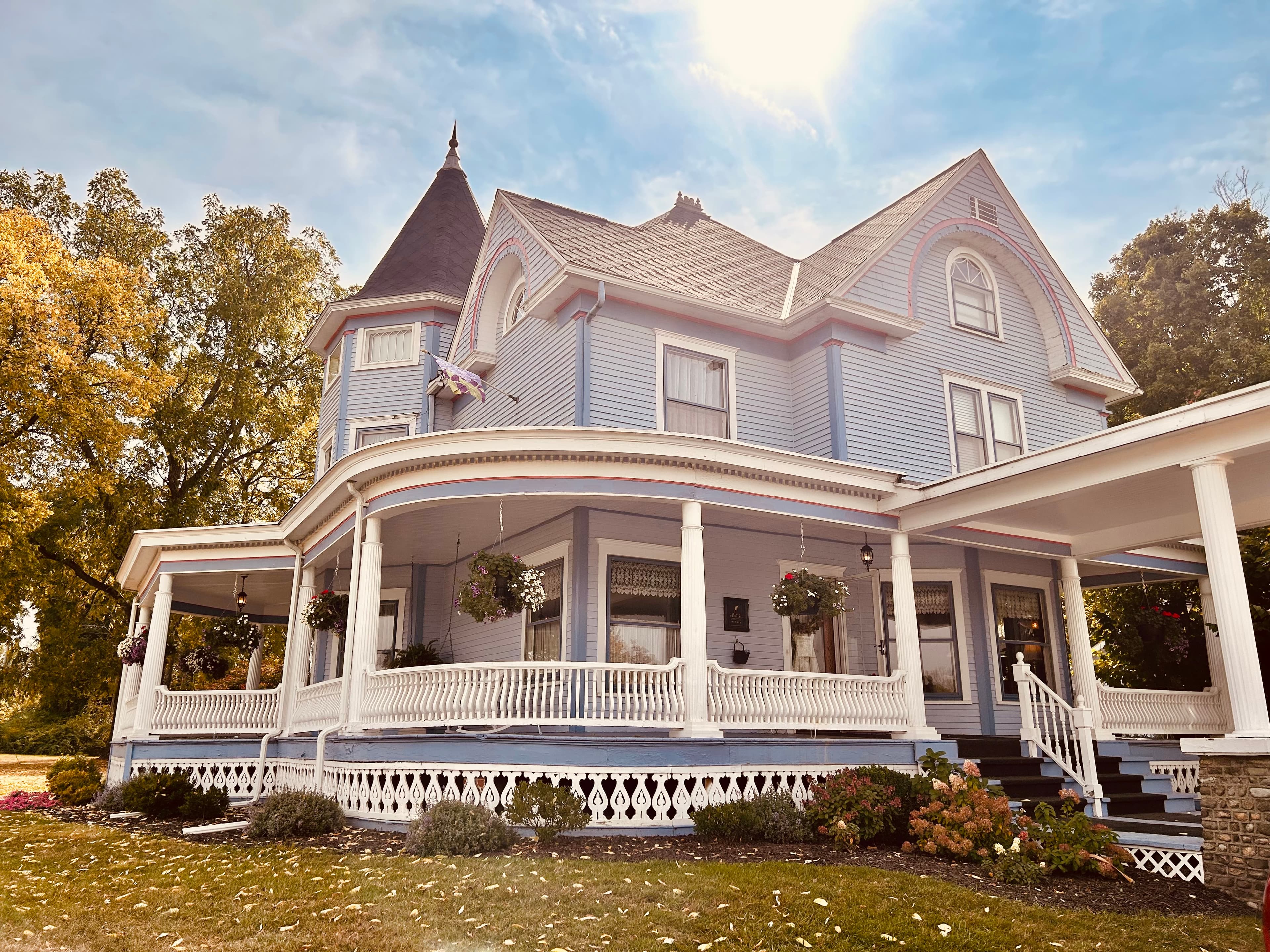 A beautifully ornate blue Victorian house with a turret and a wraparound porch.