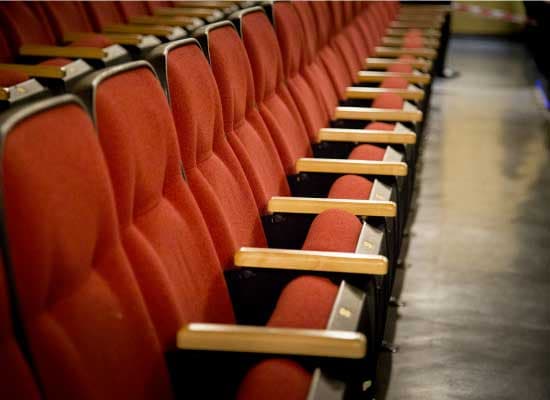 A row of red theater seats with wooden armrests.