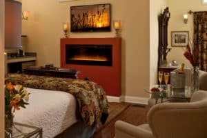 Cozy hotel room featuring a bed, a modern fireplace, and a seating area with champagne.