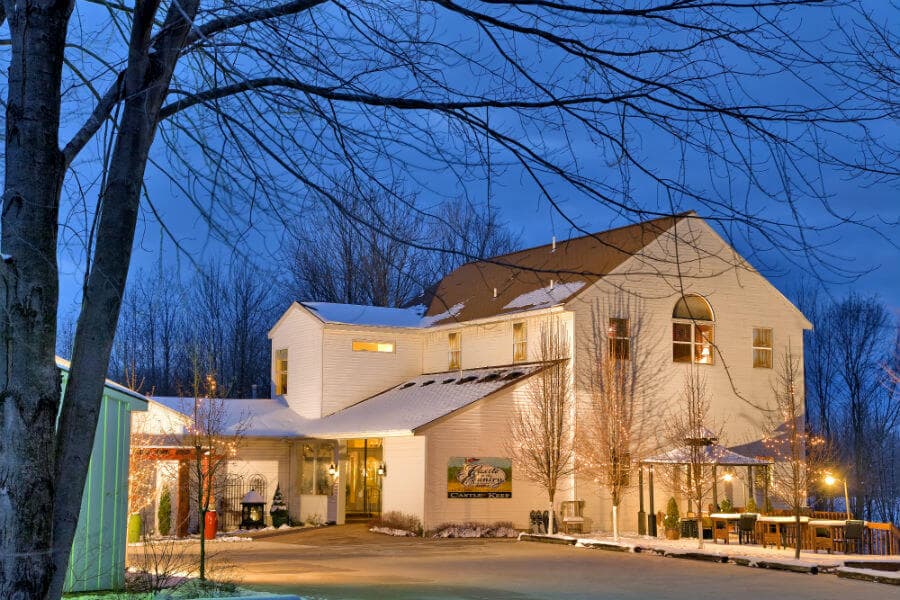 A modern white building with a sloped roof and surrounding trees, illuminated at dusk.