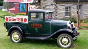 A vintage green pickup truck with a sign for "Cider Mill" parked in front of a rustic building.