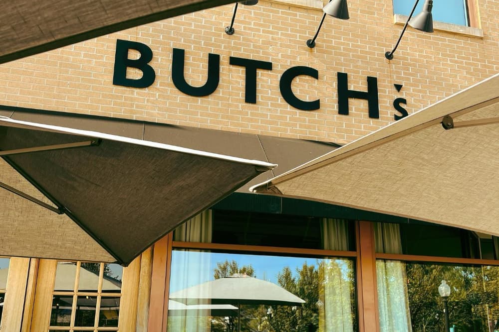 Signage of "BUTCH's" on a brick building, partially shaded by awnings.