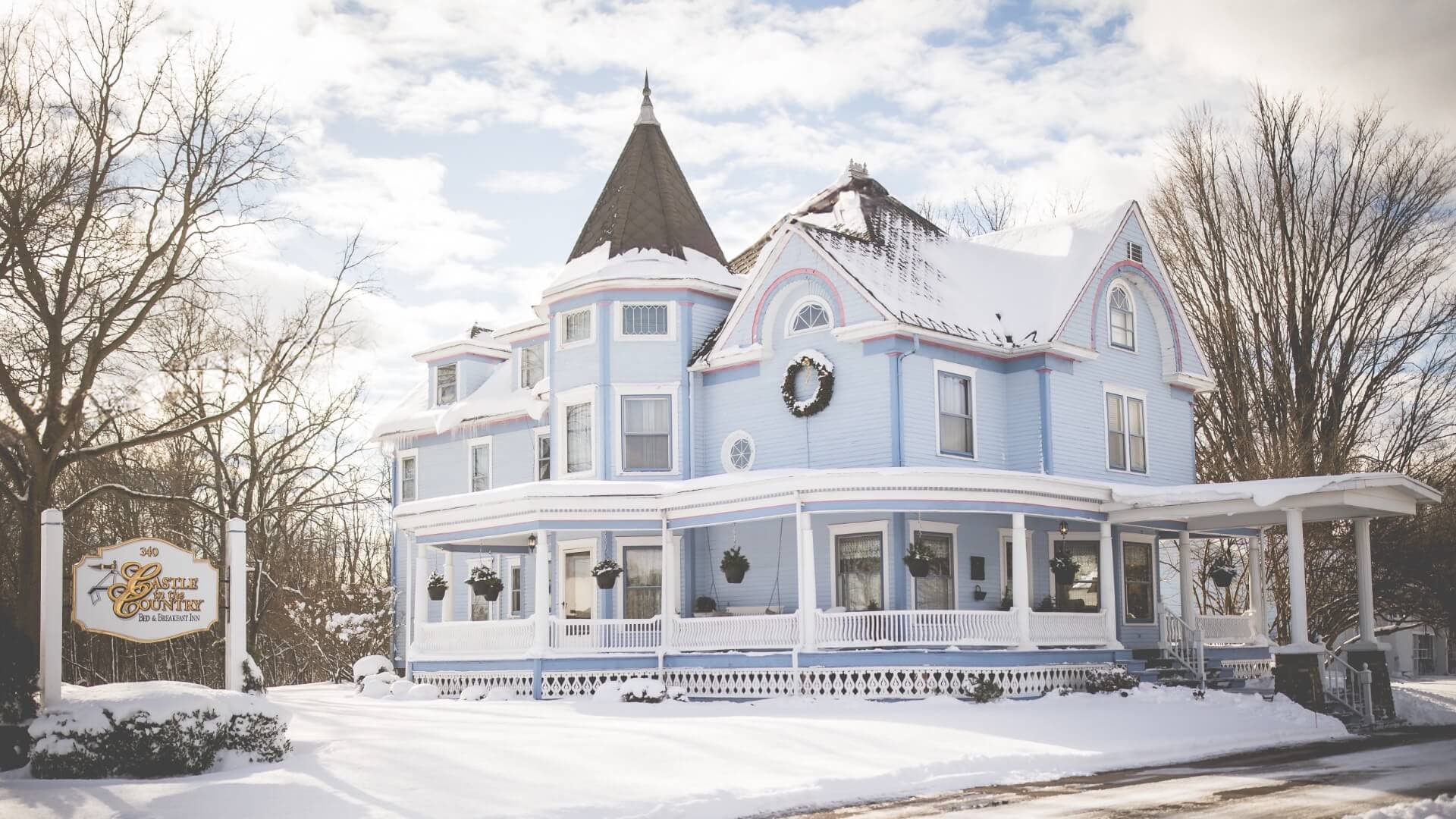 A charming blue Victorian house covered in snow.