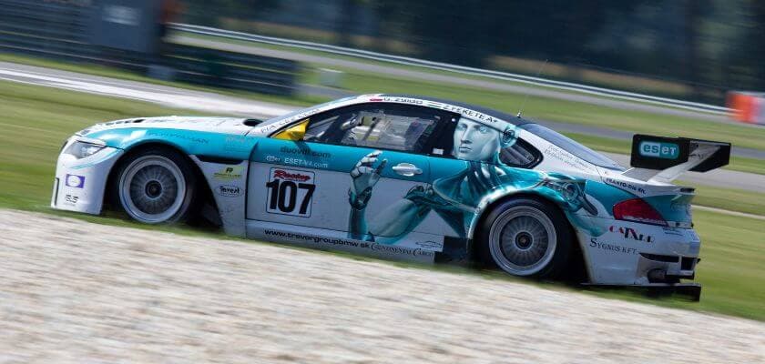 A race car with a turquoise and white design featuring a futuristic graphic is speeding around a track.