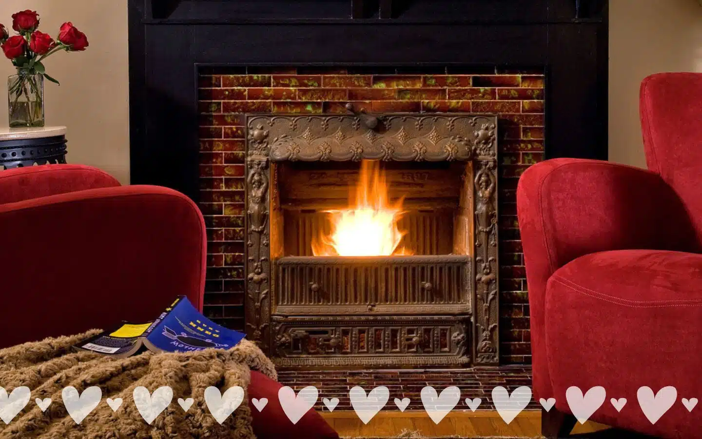 A cozy living room with a glowing fireplace and red armchairs.