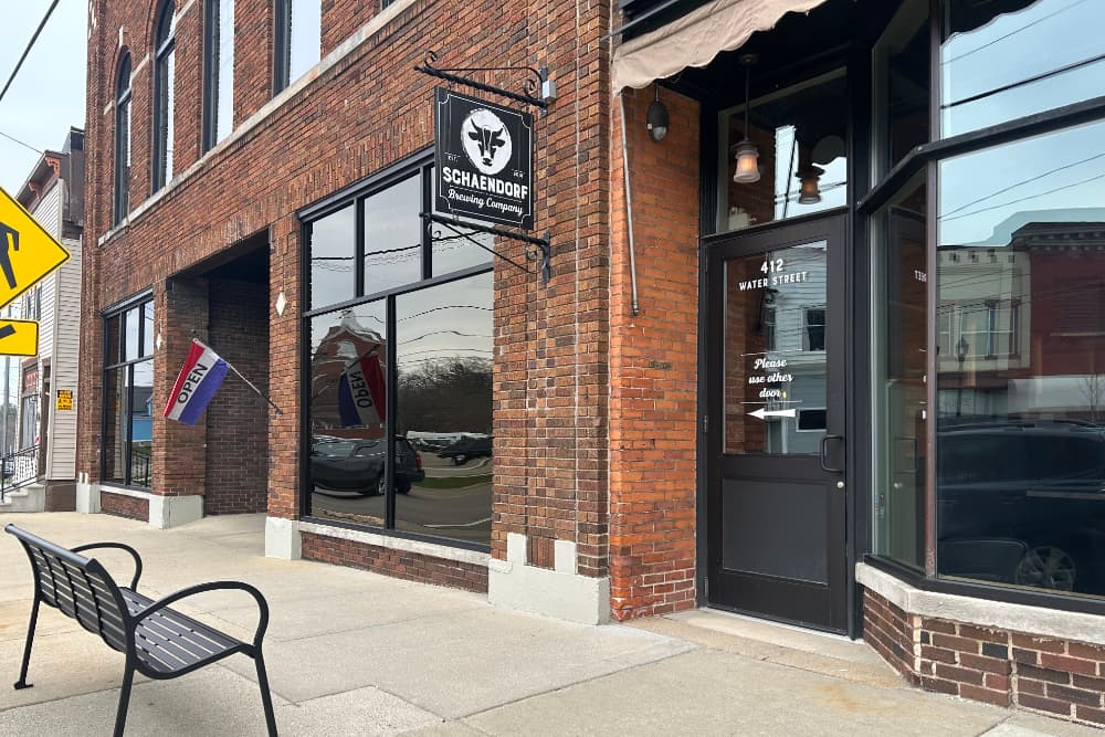 Exterior view of the Schaendorf Brewing Company with an open sign and a bench outside.