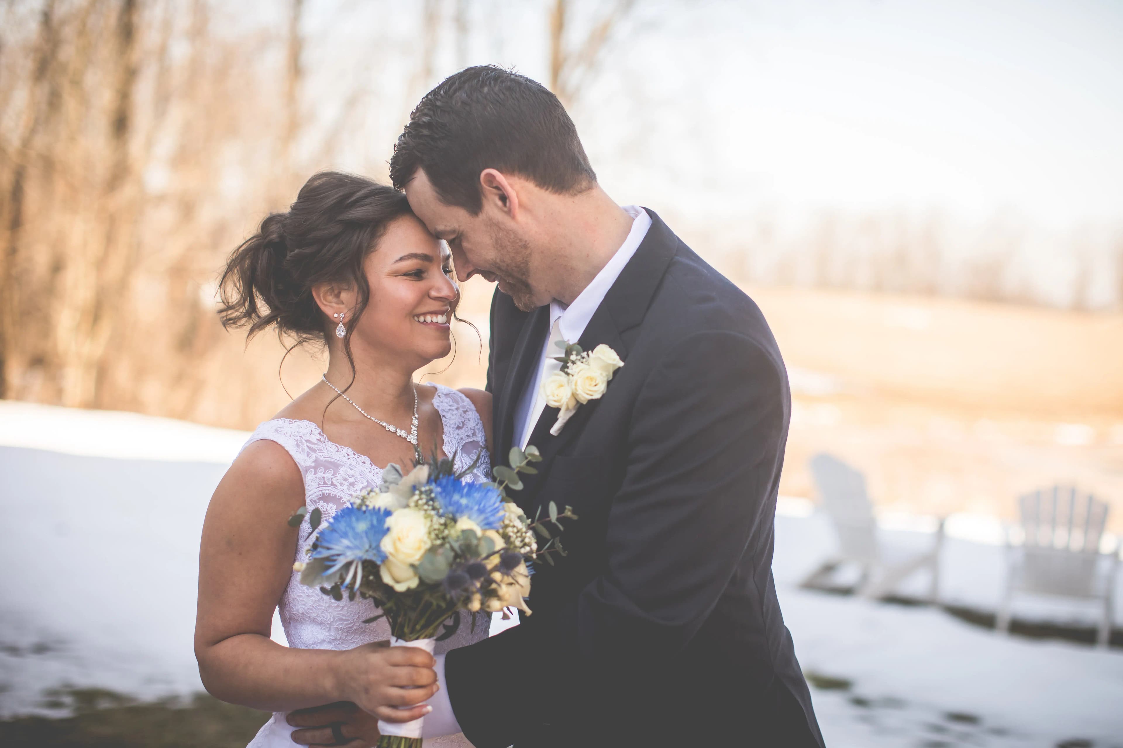 A happy couple embraces, smiling joyfully while holding a bouquet in a snowy outdoor setting.