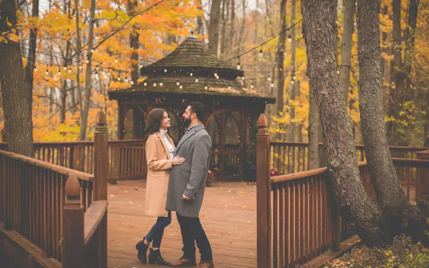 A couple stands on a wooden deck surrounded by autumn trees, gazing lovingly at each other. A couple stands on a wooden deck surrounded by autumn trees, gazing lovingly at each other.