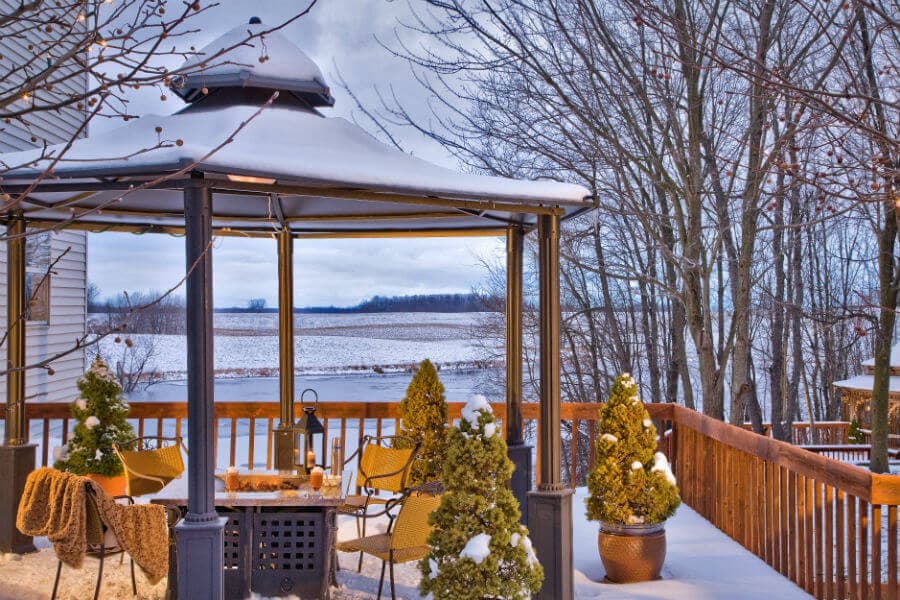 A snow-covered gazebo with seating overlooks a snowy landscape and bare trees.