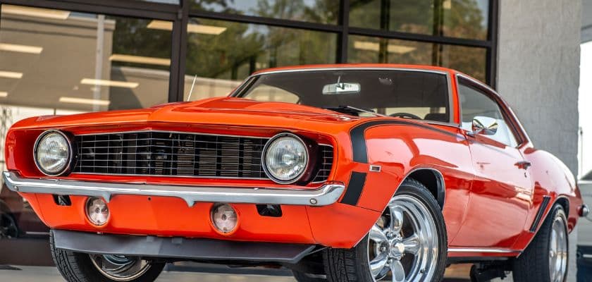 An orange 1969 Chevrolet Camaro parked in front of a modern building.