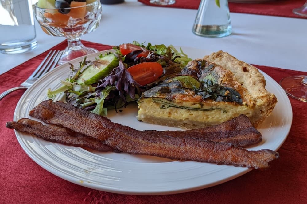 A plate of quiche accompanied by salad and crispy bacon strips.