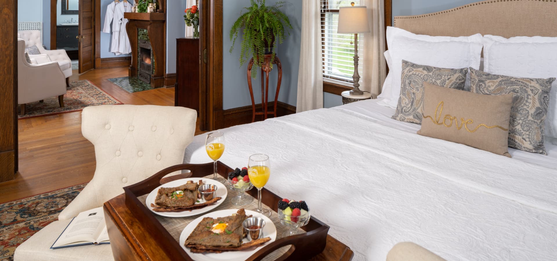 A beautifully decorated bedroom featuring a cozy bed, dining table with breakfast, and elegant furnishings.