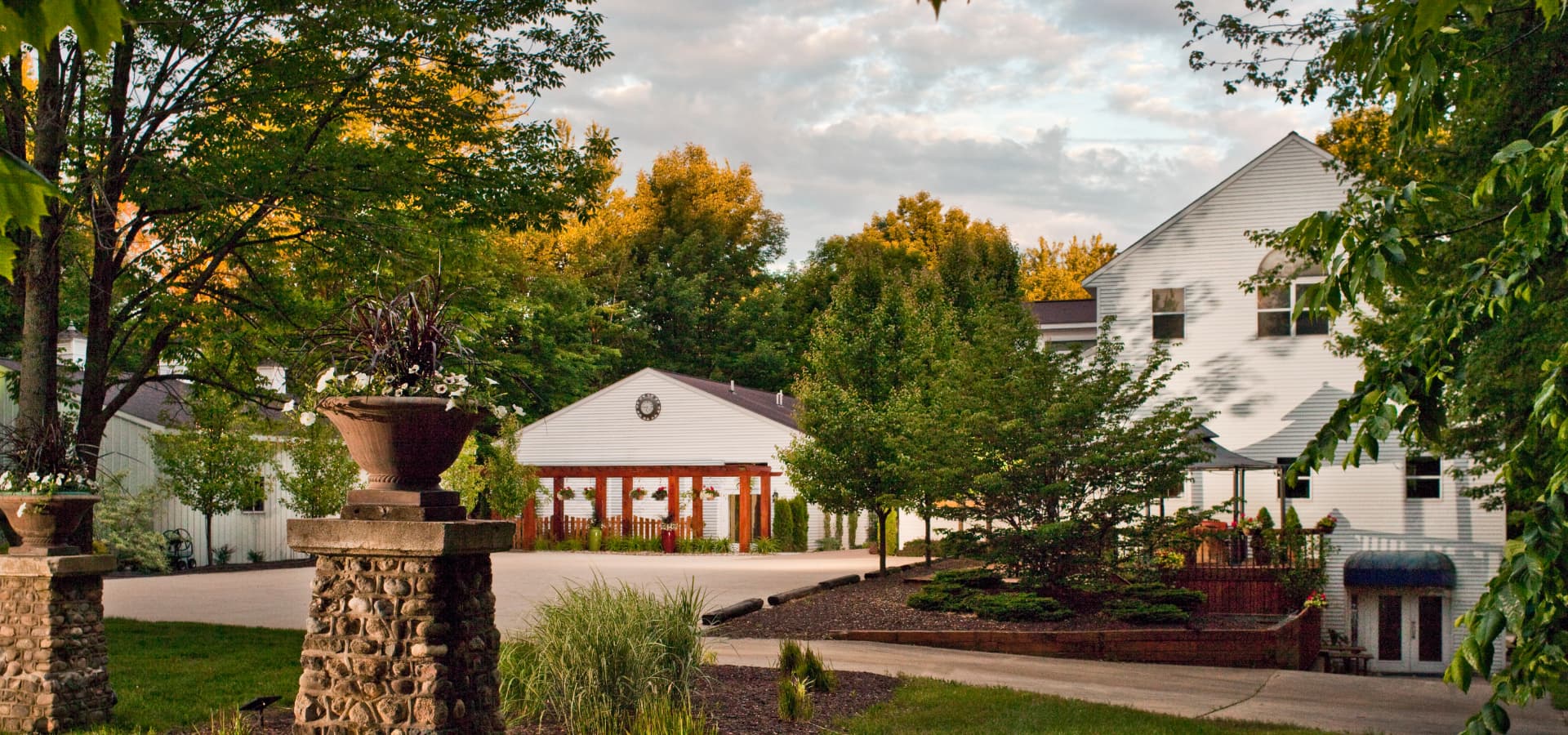 A landscaped home exterior with stone planters, greenery, and a large driveway under a partly cloudy sky.
