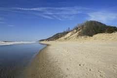 Scenic beach with a calm river and sand dunes under a clear blue sky.