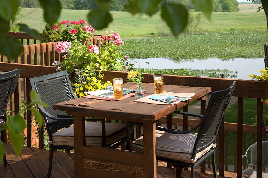A cozy outdoor dining table set with drinks and surrounded by vibrant flowers, overlooking a serene landscape.
