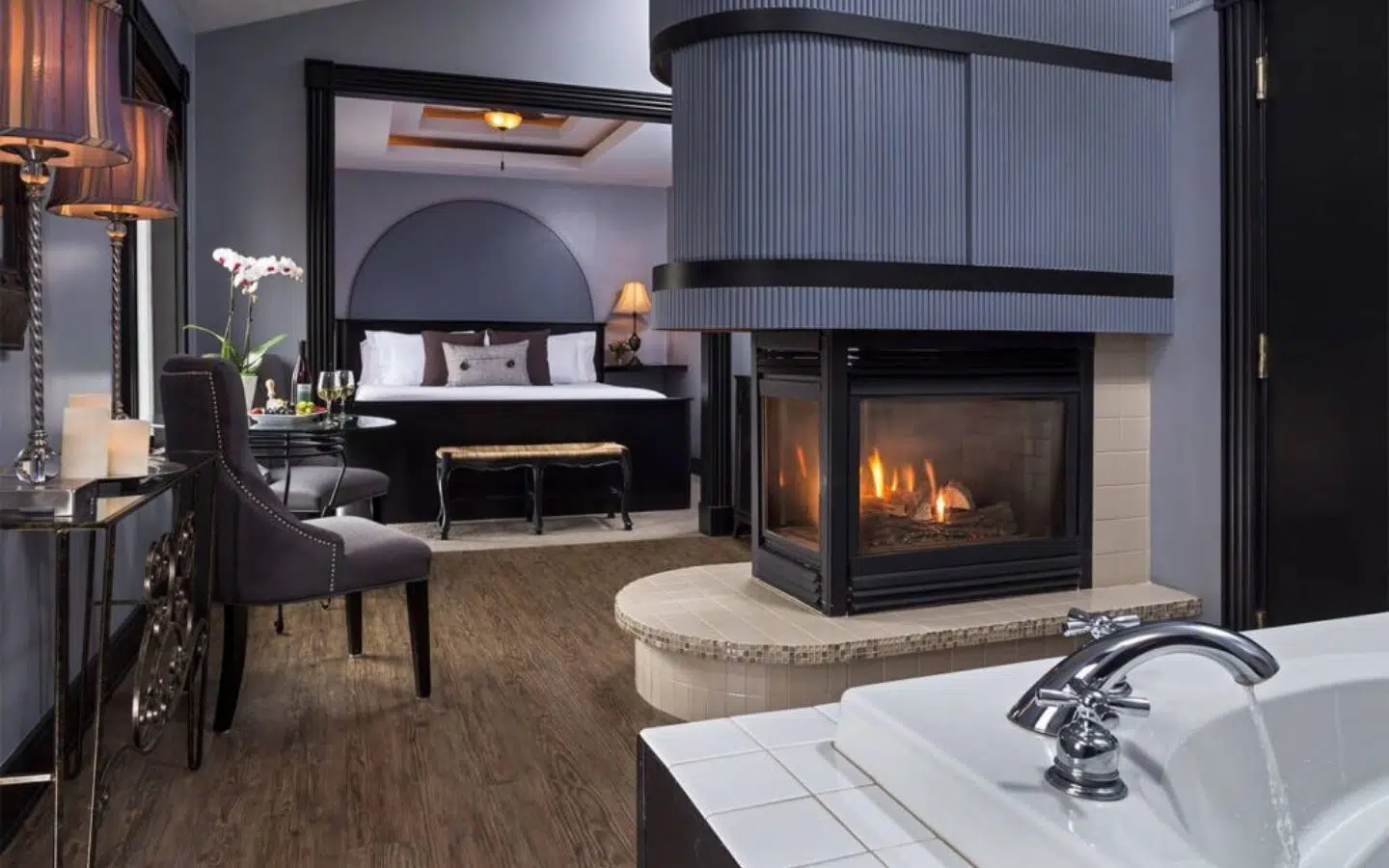 A cozy hotel room featuring a fireplace, seating area, and a view of the bed.