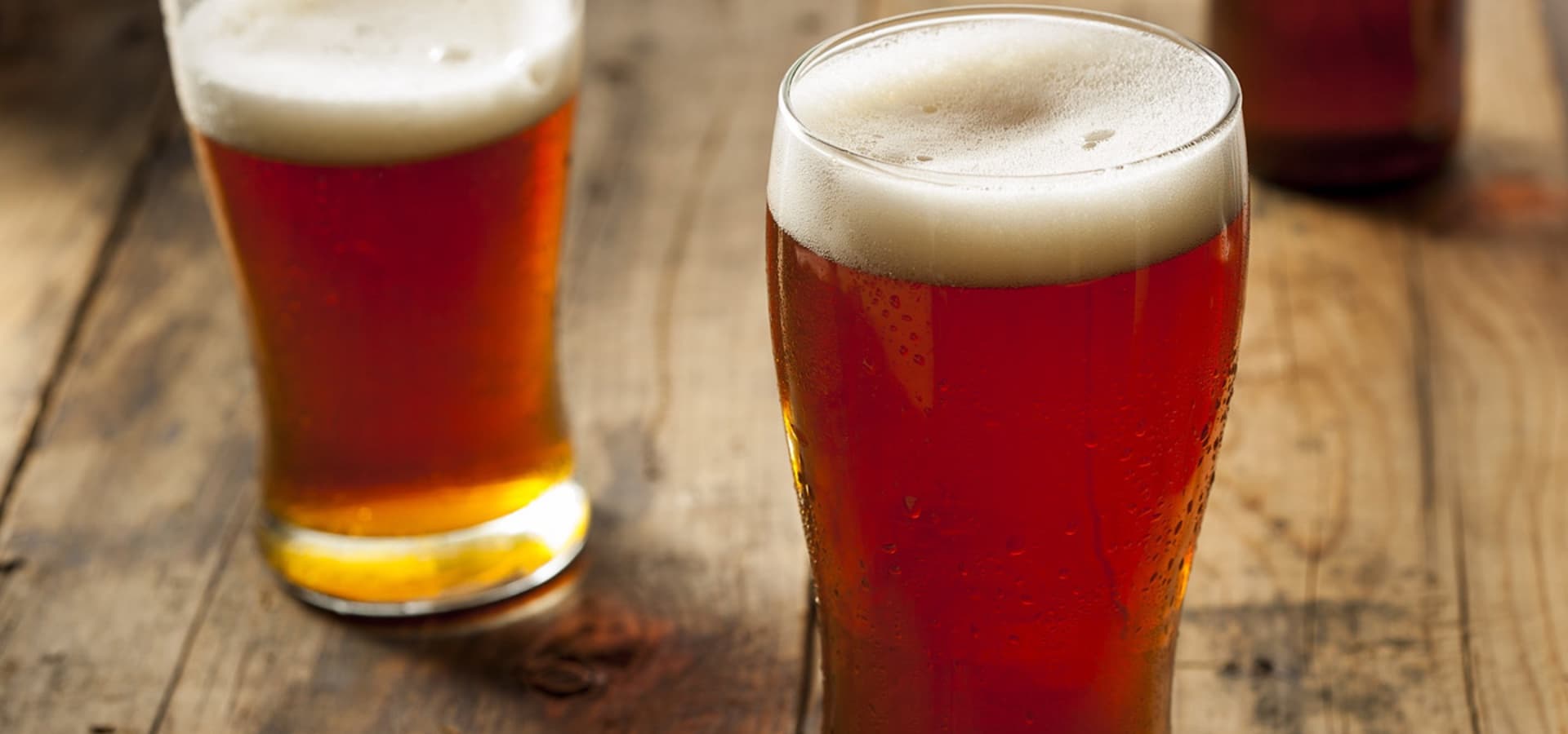 Two glasses of amber beer with frothy tops on a wooden table.