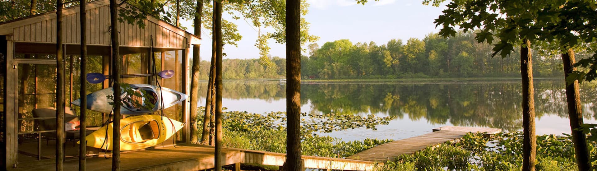 A lakeside cabin with kayaks stored on a deck surrounded by trees and reflecting water.