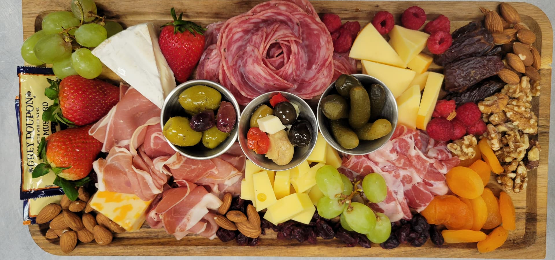 A vibrant charcuterie board featuring various cheeses, meats, fruits, olives, nuts, and dried fruits arranged on a wooden platter.