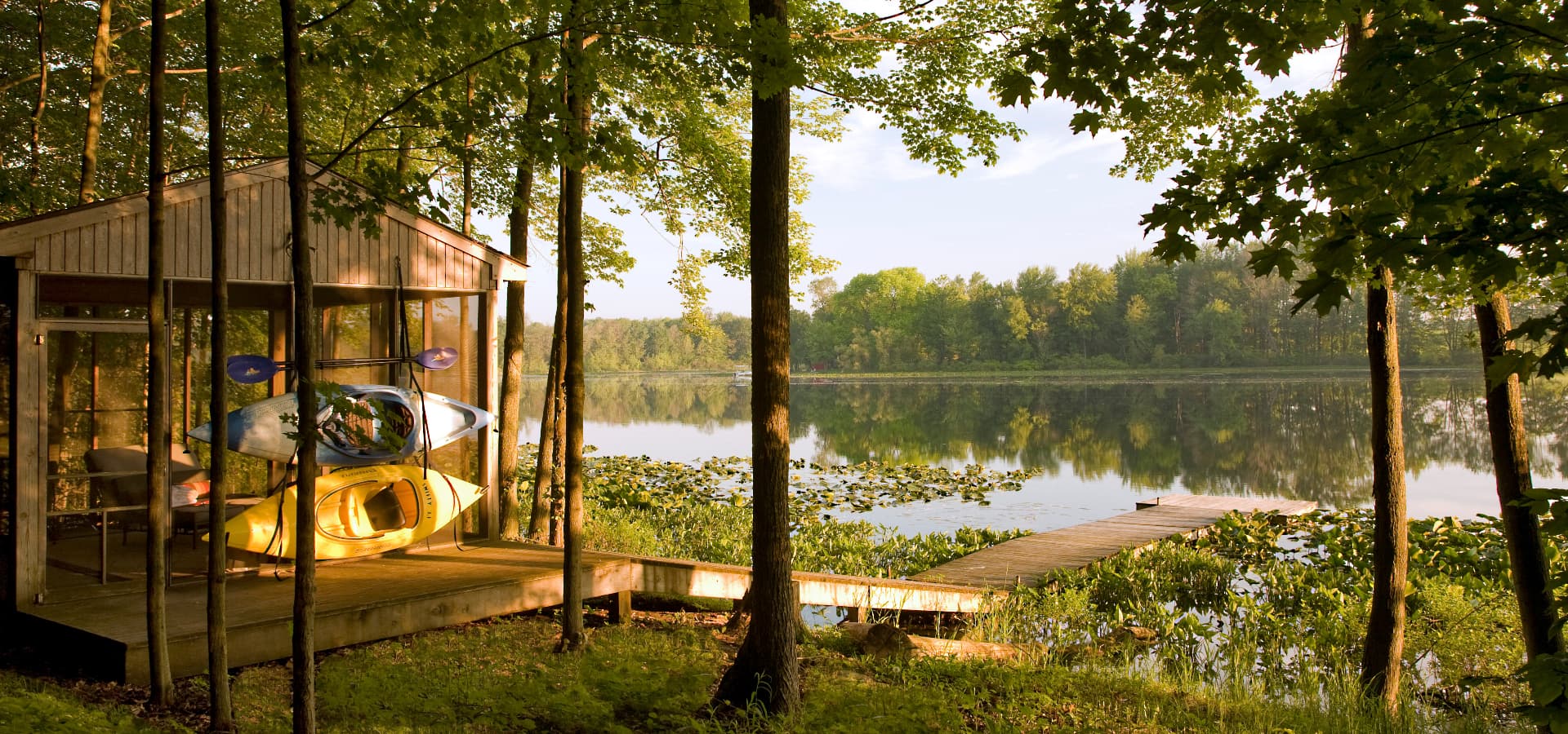 A kayak rests on a wooden dock by a serene lake surrounded by lush trees.