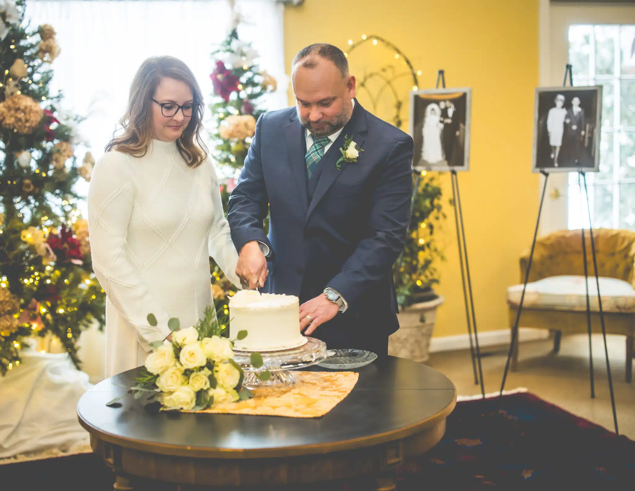 A couple cuts their wedding cake surrounded by festive decorations and photographs.