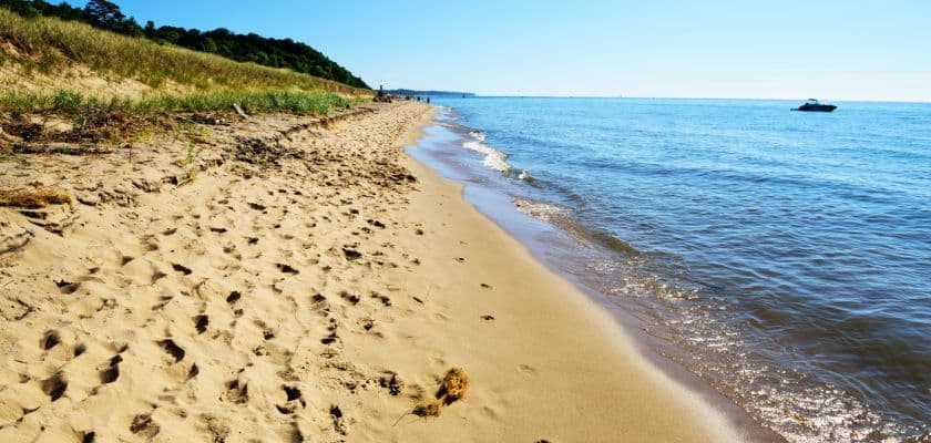 A sandy beach with footprints leading to calm water under a clear blue sky.