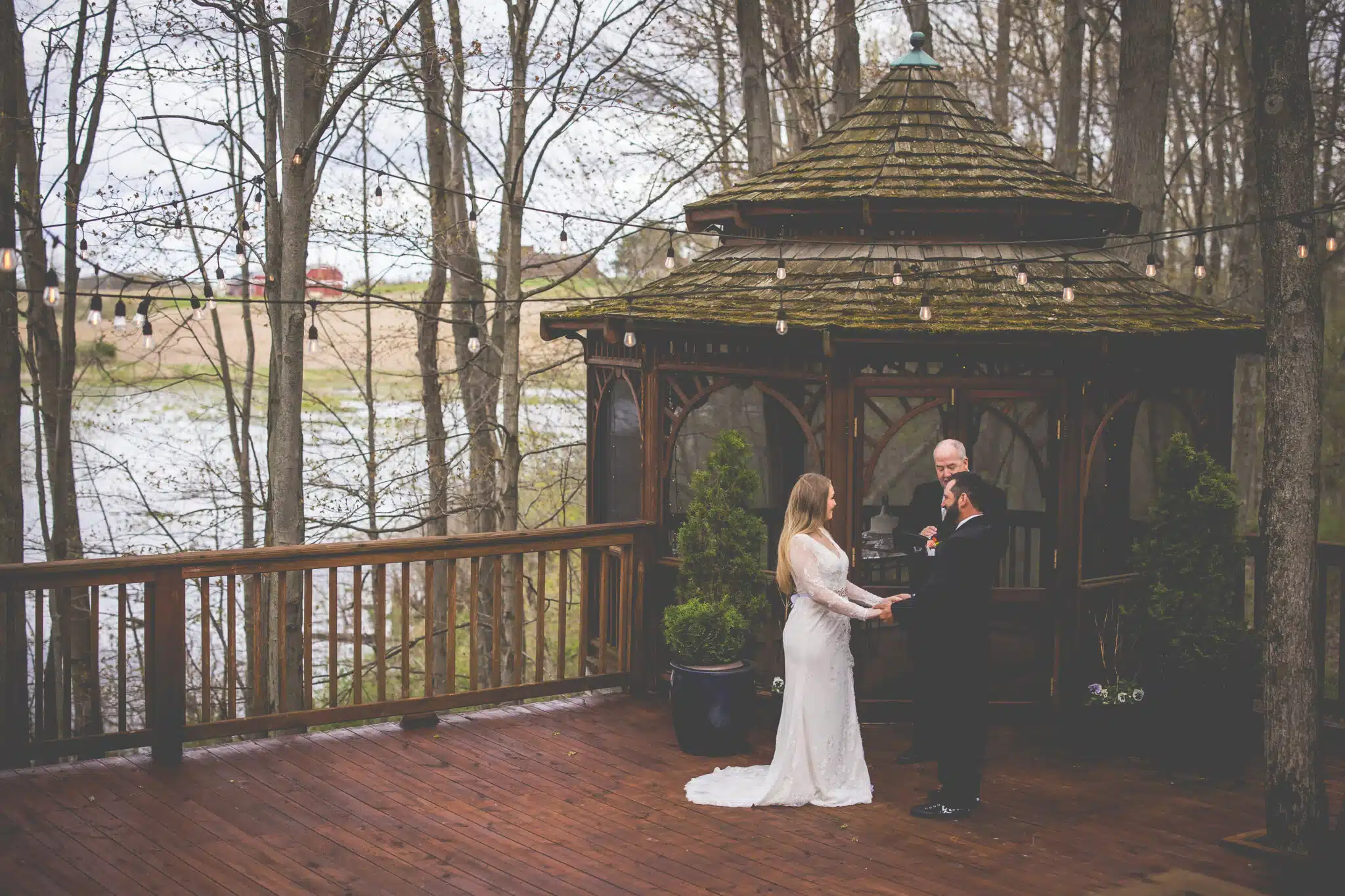 A couple exchanges vows under a gazebo in a serene outdoor setting.