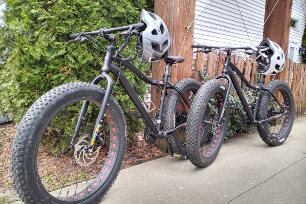 Two fat bikes with helmets parked near a green bush.