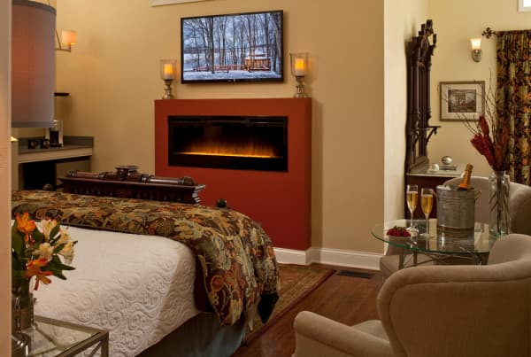 A cozy, elegantly decorated hotel room featuring a fireplace, television, and floral arrangements.