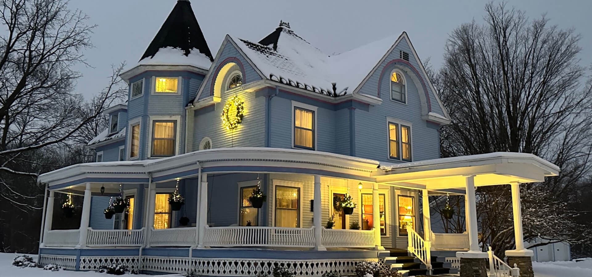 A charming blue Victorian house adorned with winter lights, surrounded by snow.