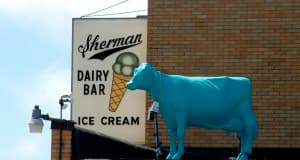 A blue cow statue stands atop a sign for Sherman's Dairy Bar featuring an ice cream cone.