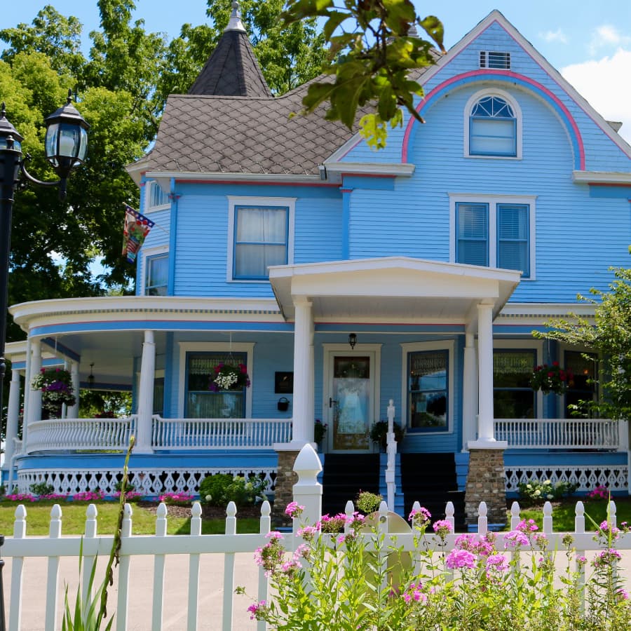 A charming blue Victorian-style house with a wraparound porch and colorful flower baskets.