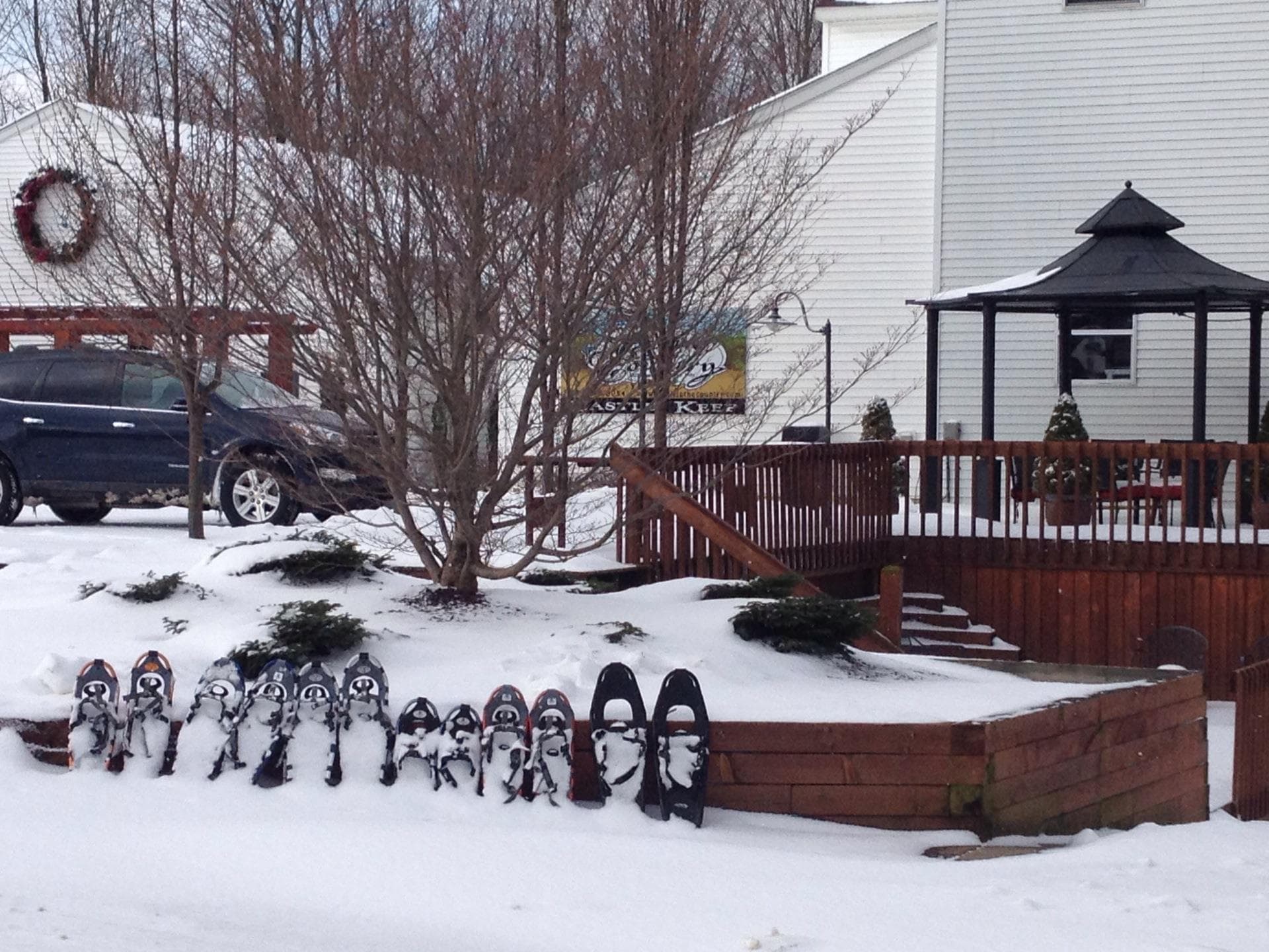A row of snowshoes is lined up on a snowy landscape in front of a wooden deck and gazebo.