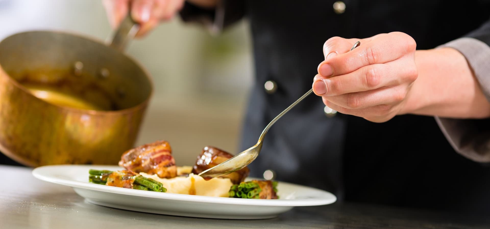 A chef drizzles sauce over a plated dish featuring meat and vegetables.