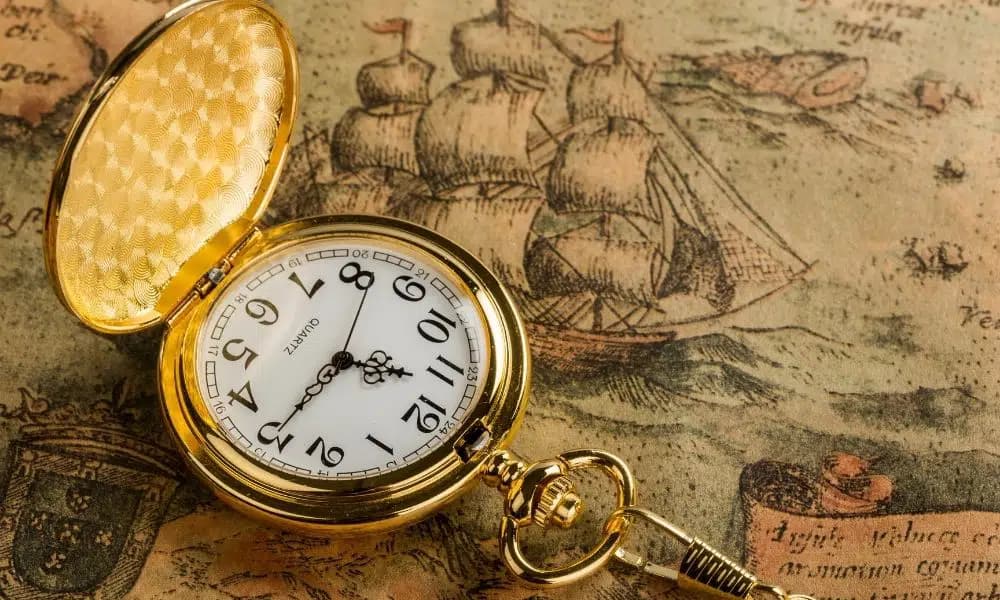 A gold pocket watch rests on an antique map featuring sailing ships. A gold pocket watch rests on an antique map featuring sailing ships.