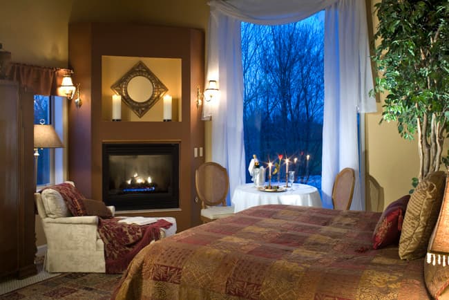 A cozy bedroom with a fireplace, a large window, and a small dining table set for two.