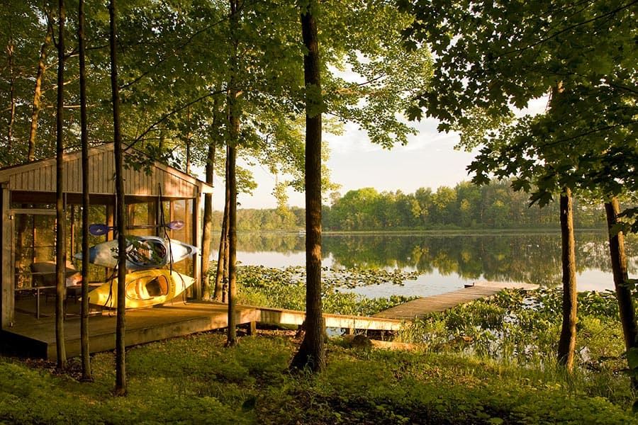 A serene lakeside scene featuring a wooden dock, a kayak, and lush greenery.