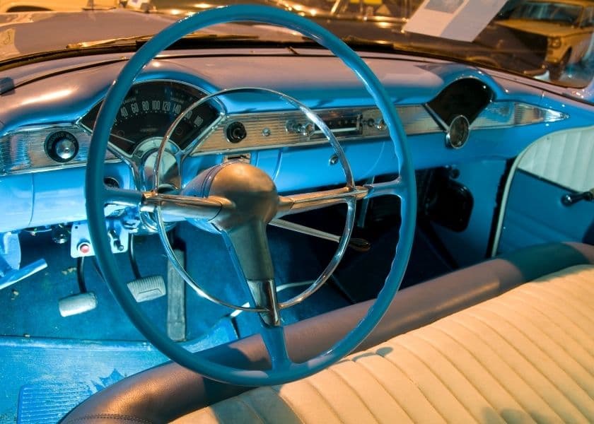 Close-up of a vintage car interior featuring a blue dashboard and steering wheel.