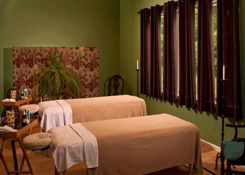 A serene spa room with two massage tables, surrounded by green walls and soft lighting. A serene spa room with two massage tables, surrounded by green walls and soft lighting.
