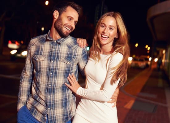 A smiling couple walks closely together on a city street at night.