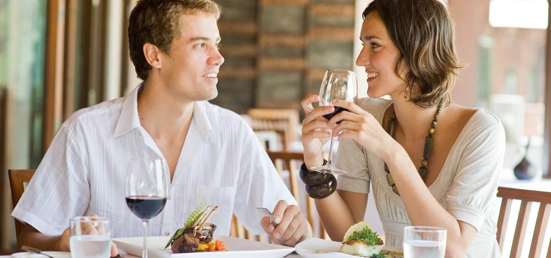 A couple enjoys a meal together at a restaurant, sharing smiles and glasses of wine.