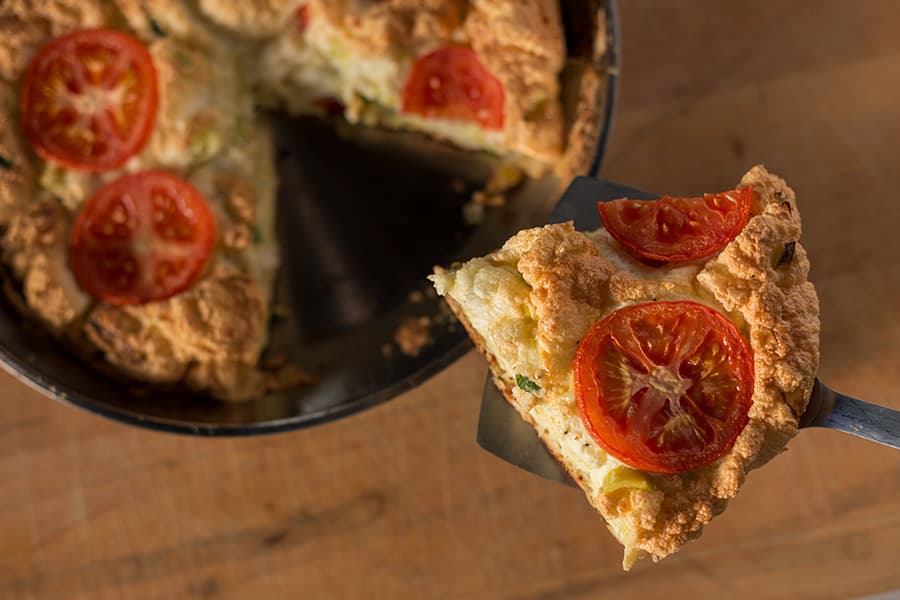 A slice of fluffy pie topped with sliced tomatoes, lifted from a round baking dish.