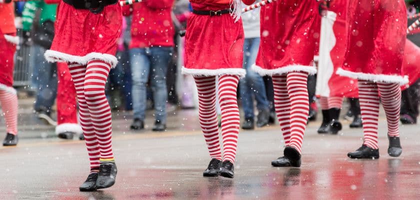 A group of performers in red costumes and striped stockings marching in the snow.
