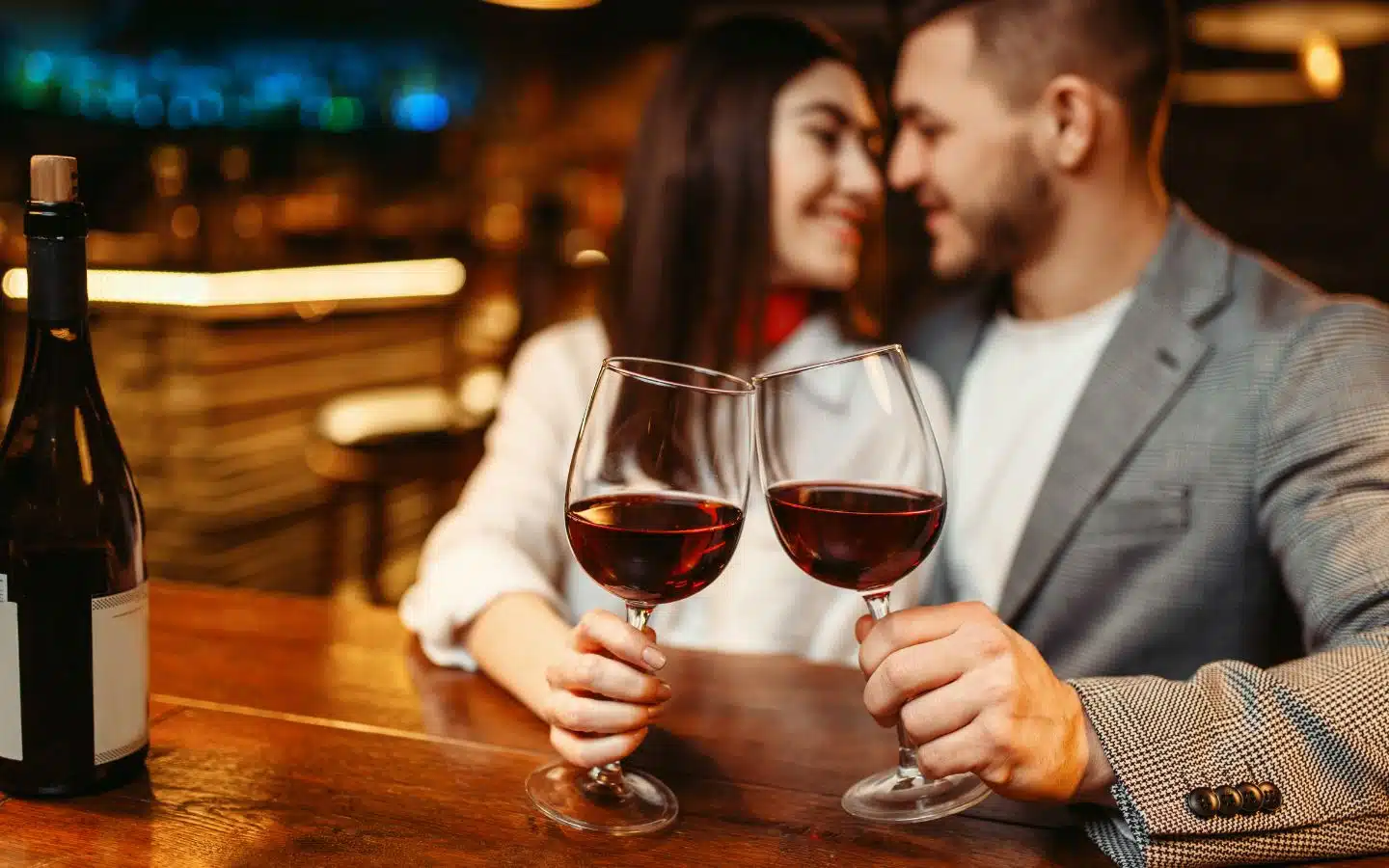 A couple clinks wine glasses together at a cozy bar.